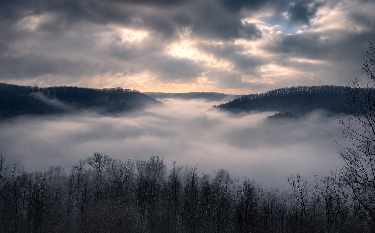 Fog settling through wooded Tennessee hills beneath a dramatic sky